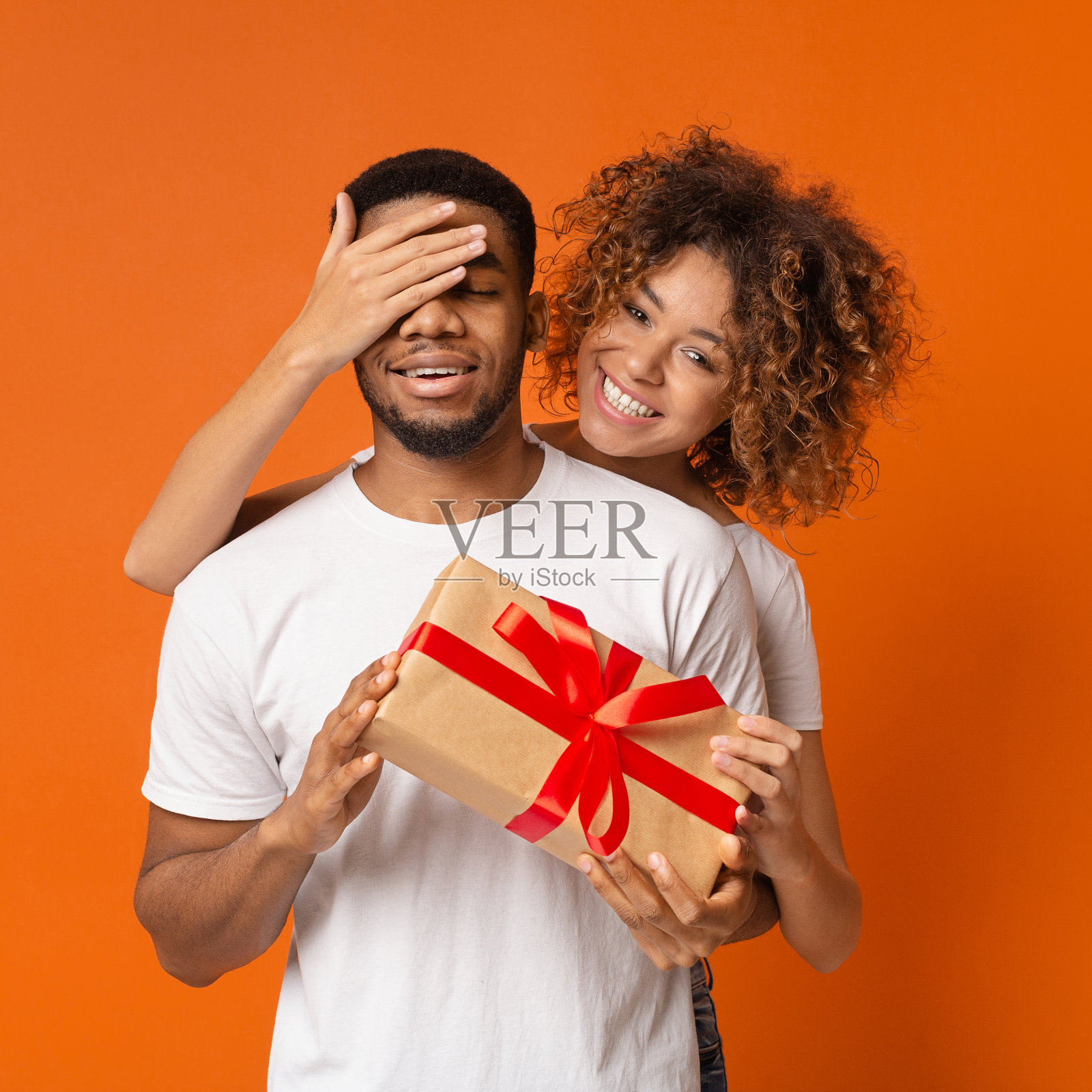 可爱的非洲女孩覆盖她的男朋友的眼睛和给他的礼物照片摄影图片