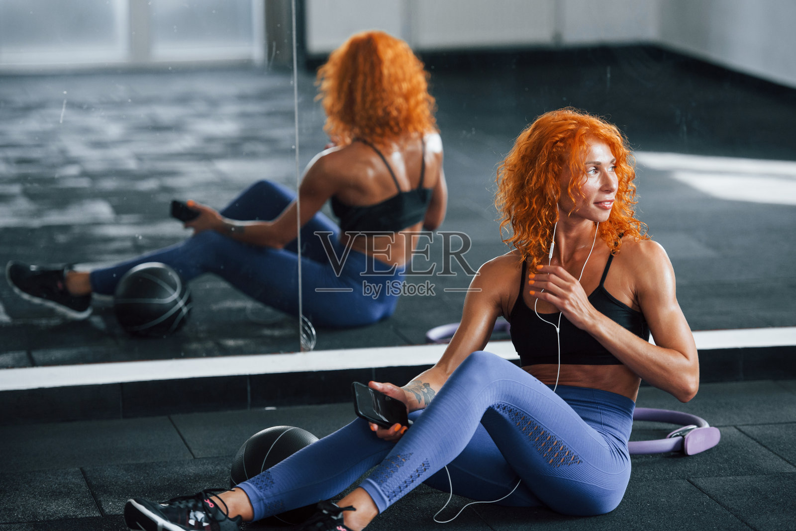 戴着耳机听音乐。喜欢运动的红发女孩白天去健身房健身。肌肉发达的身体类型照片摄影图片