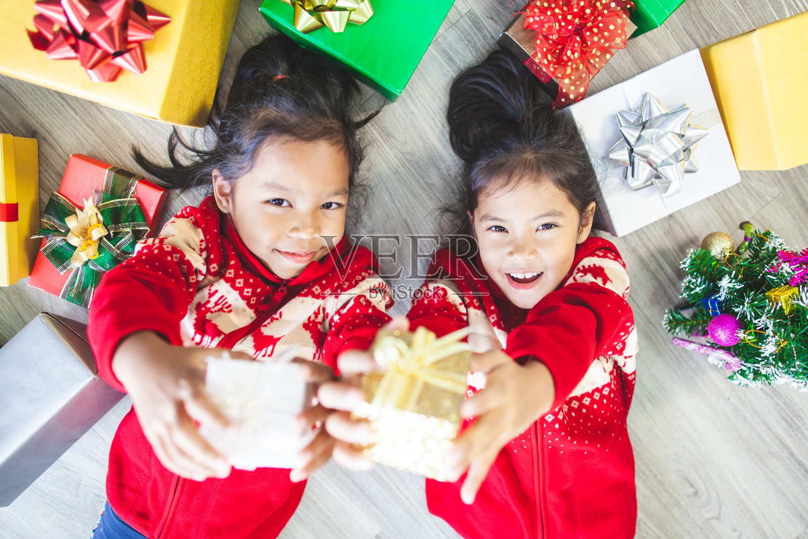 在圣诞节庆祝活动中，两个可爱的亚洲小女孩躺在地板上并赠送礼盒照片摄影图片