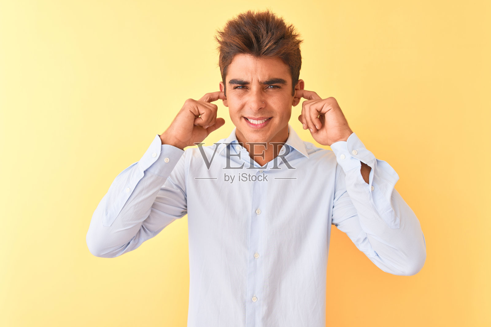 年轻英俊的商人穿着优雅的衬衫在孤立的黄色背景掩盖耳朵与手指与恼怒的表情噪音的大声音乐。聋的概念。照片摄影图片
