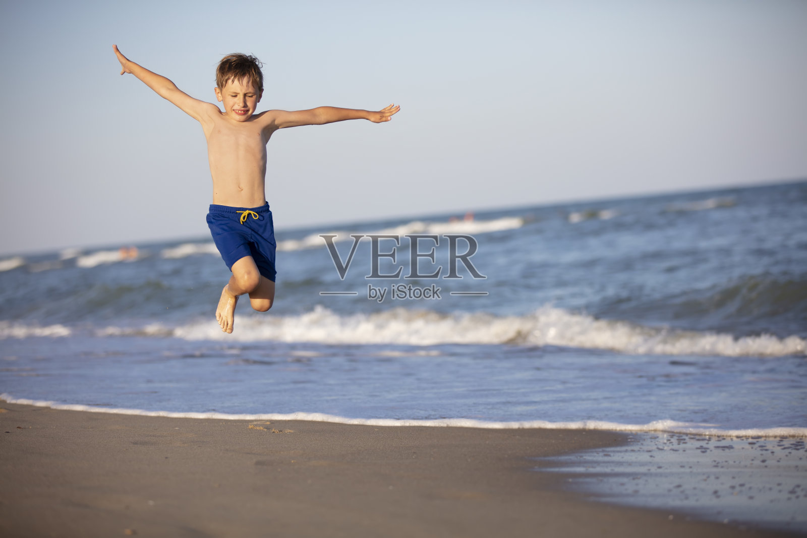 一个孩子在海滩上玩耍。一个快乐的男孩在海边跳得很高。在海滩上度过愉快的假期照片摄影图片