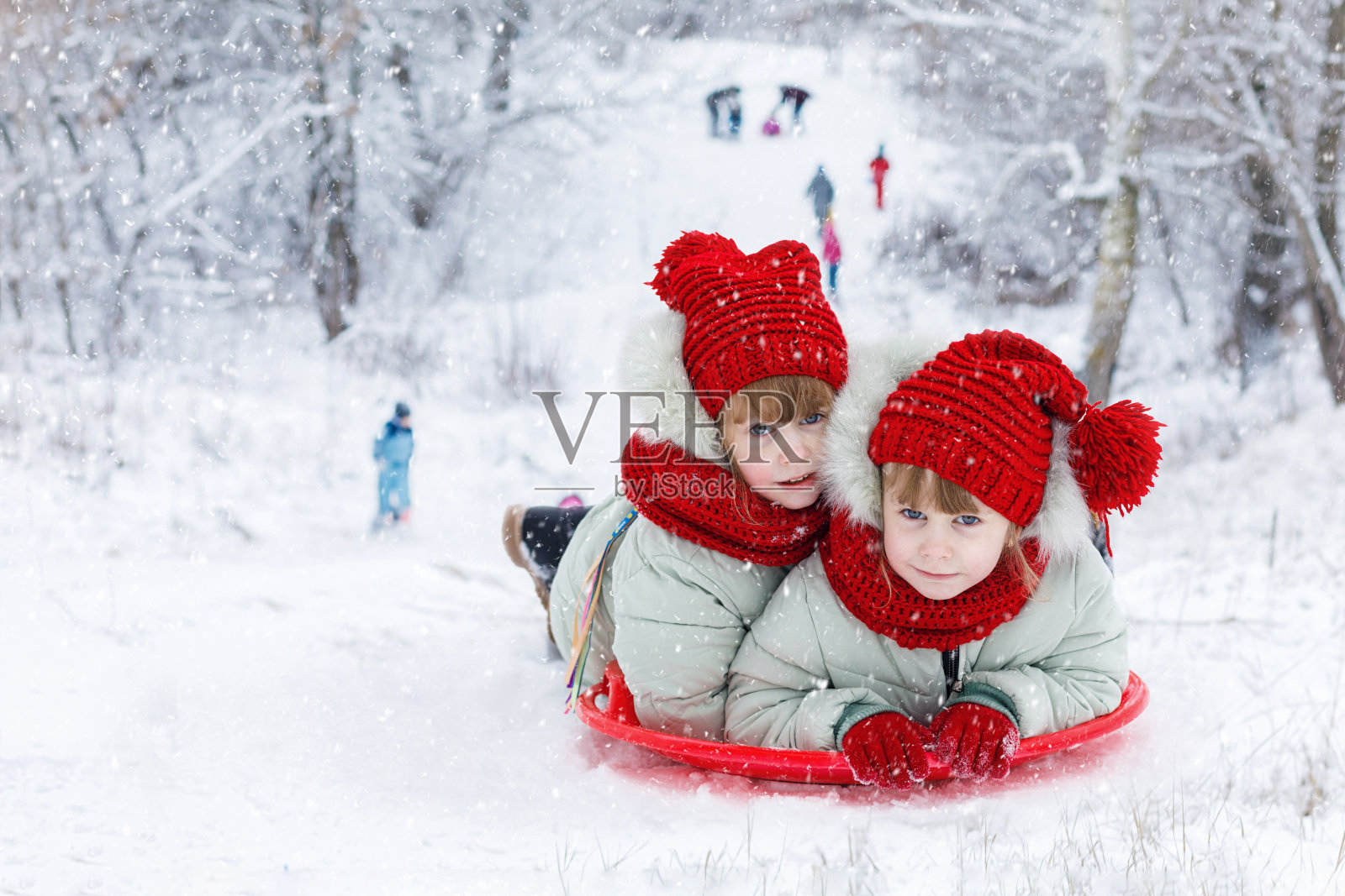 一对双胞胎姐妹骑在一座雪山上。照片摄影图片