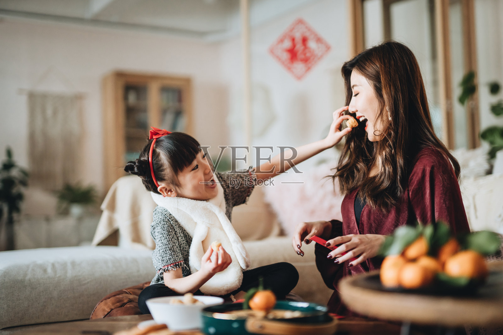 可爱的女儿在家里帮妈妈准备红包时，与妈妈分享传统小吃照片摄影图片