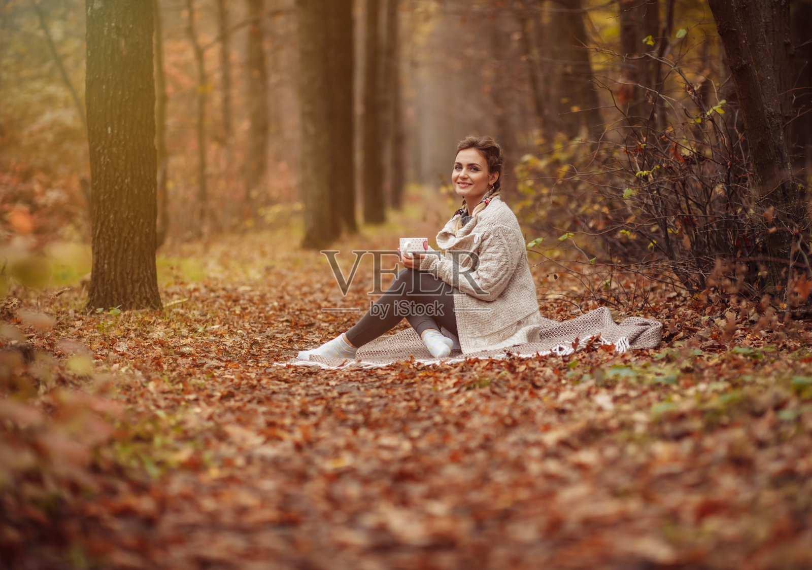 艺术肖像。年轻迷人的女子坐在格子裙上，在秋天的森林里喝茶照片摄影图片