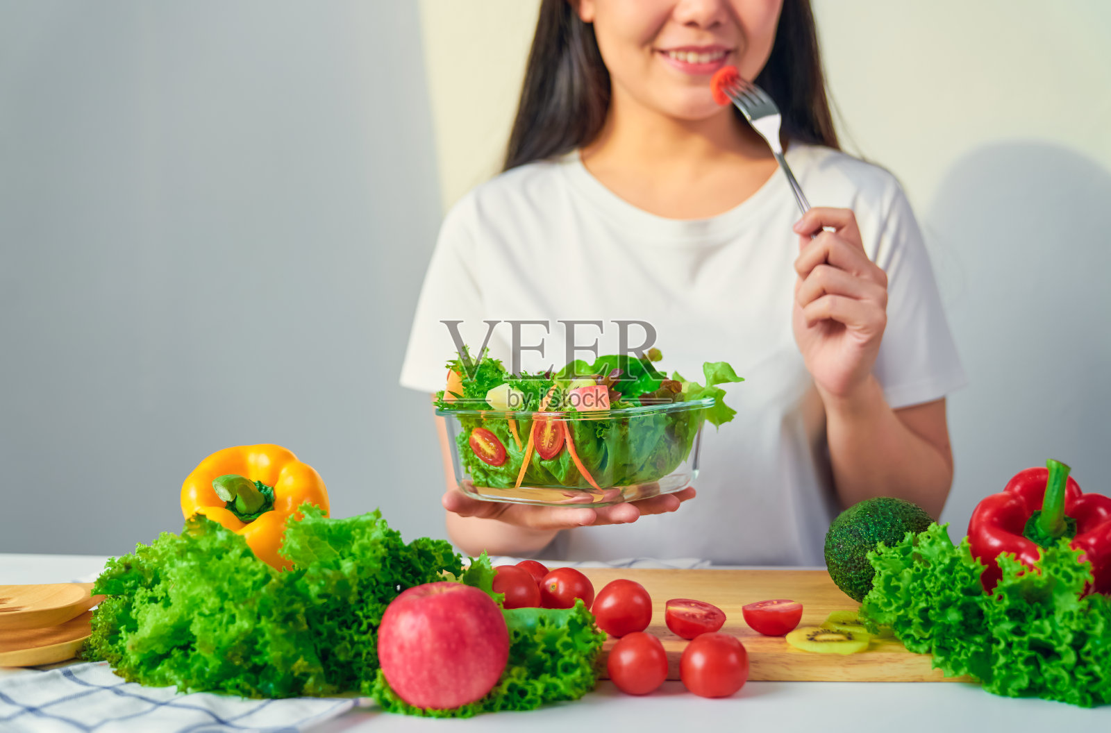 女人手里拿着沙拉碗，把吃西红柿和各种绿叶蔬菜放在家里的桌子上。照片摄影图片