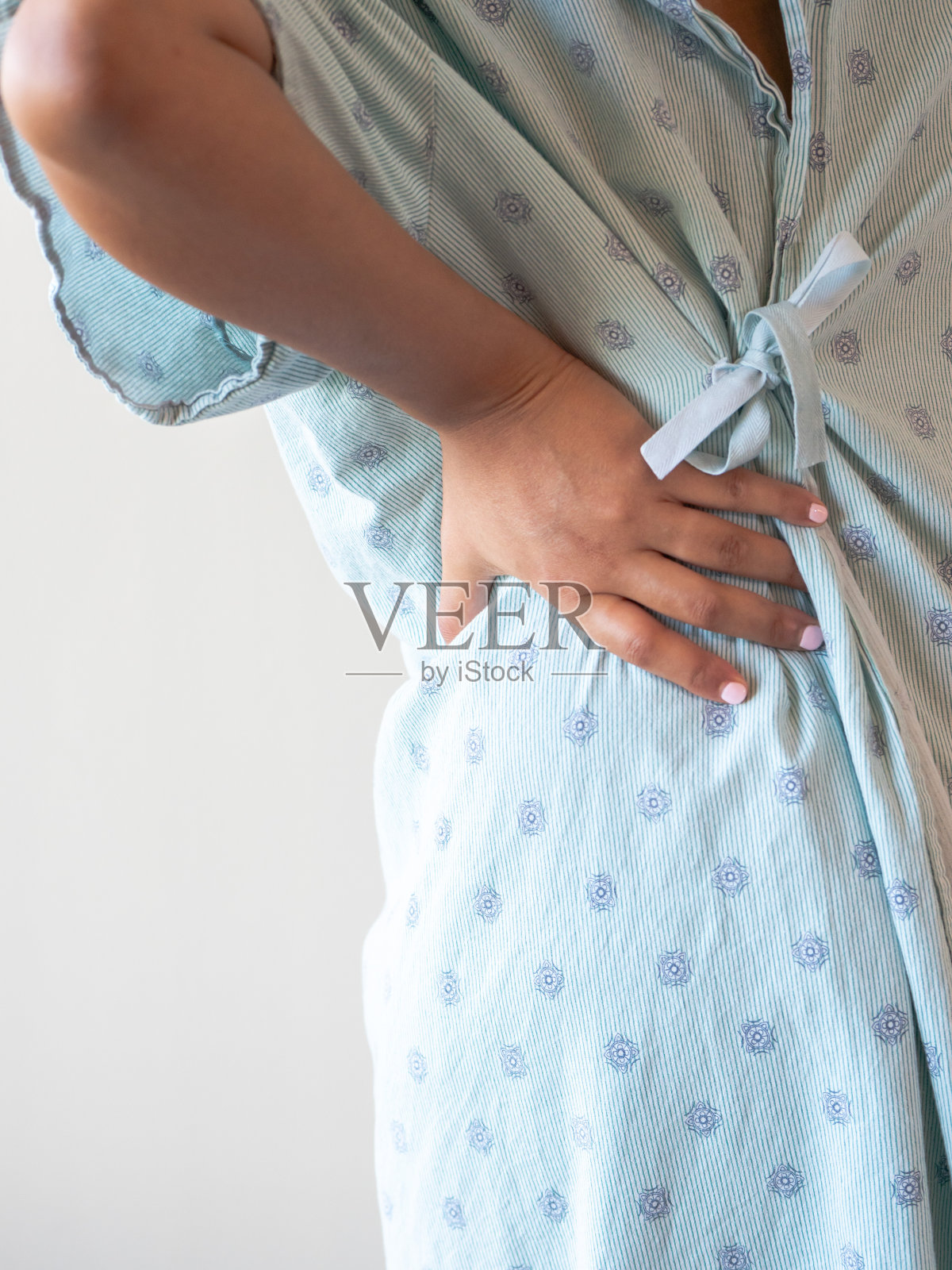这是一张近距离的照片，一位中年非裔美国混血妇女的手放在她的下背部或臀部，她穿着有图案的医院长袍，痛苦地弓着腰。照片摄影图片