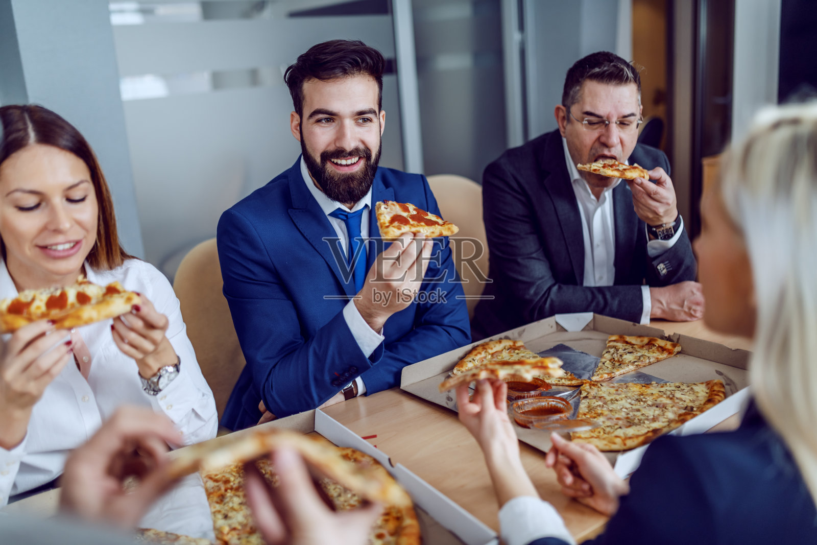 一群饥肠辘辘的商务人士坐在会议室里吃披萨当午餐。照片摄影图片