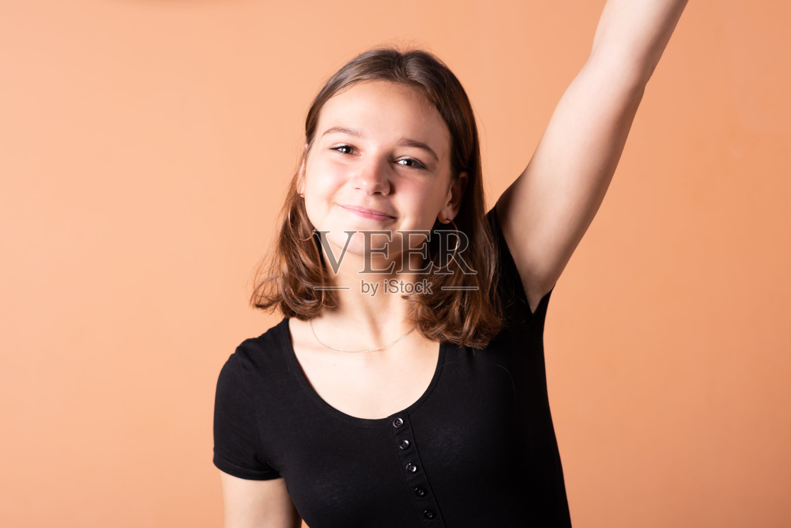 女孩挥舞着她的手，在浅橙色的背景上。照片摄影图片
