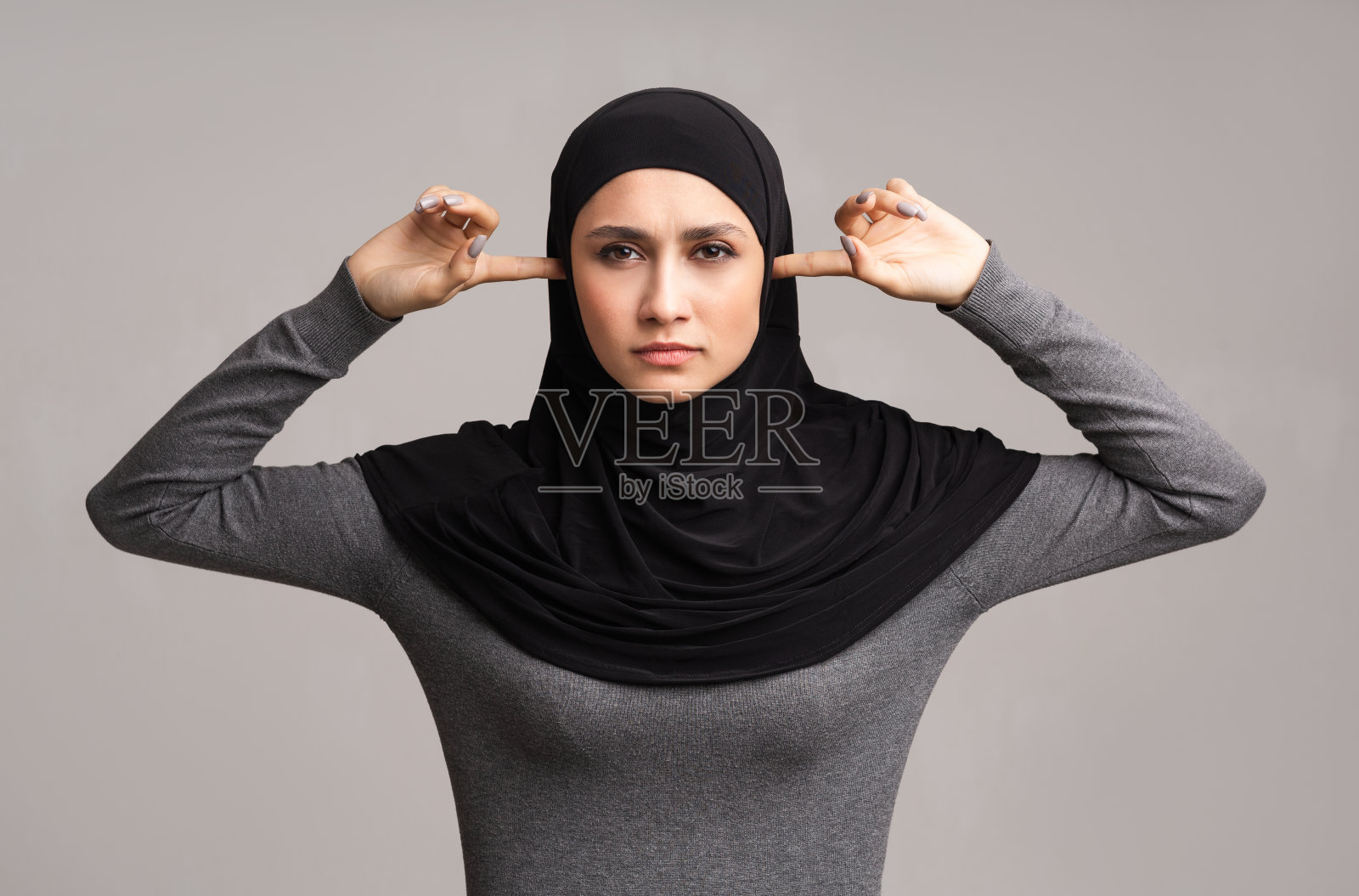 穆斯林妇女在头巾关闭耳朵与手指在灰色的背景照片摄影图片
