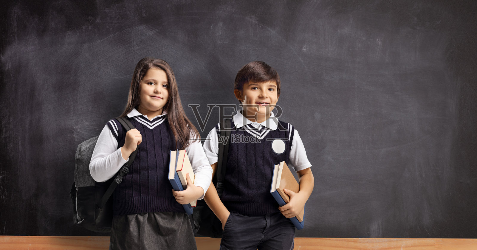 孩子们穿着校服拿着书站在黑板前照片摄影图片