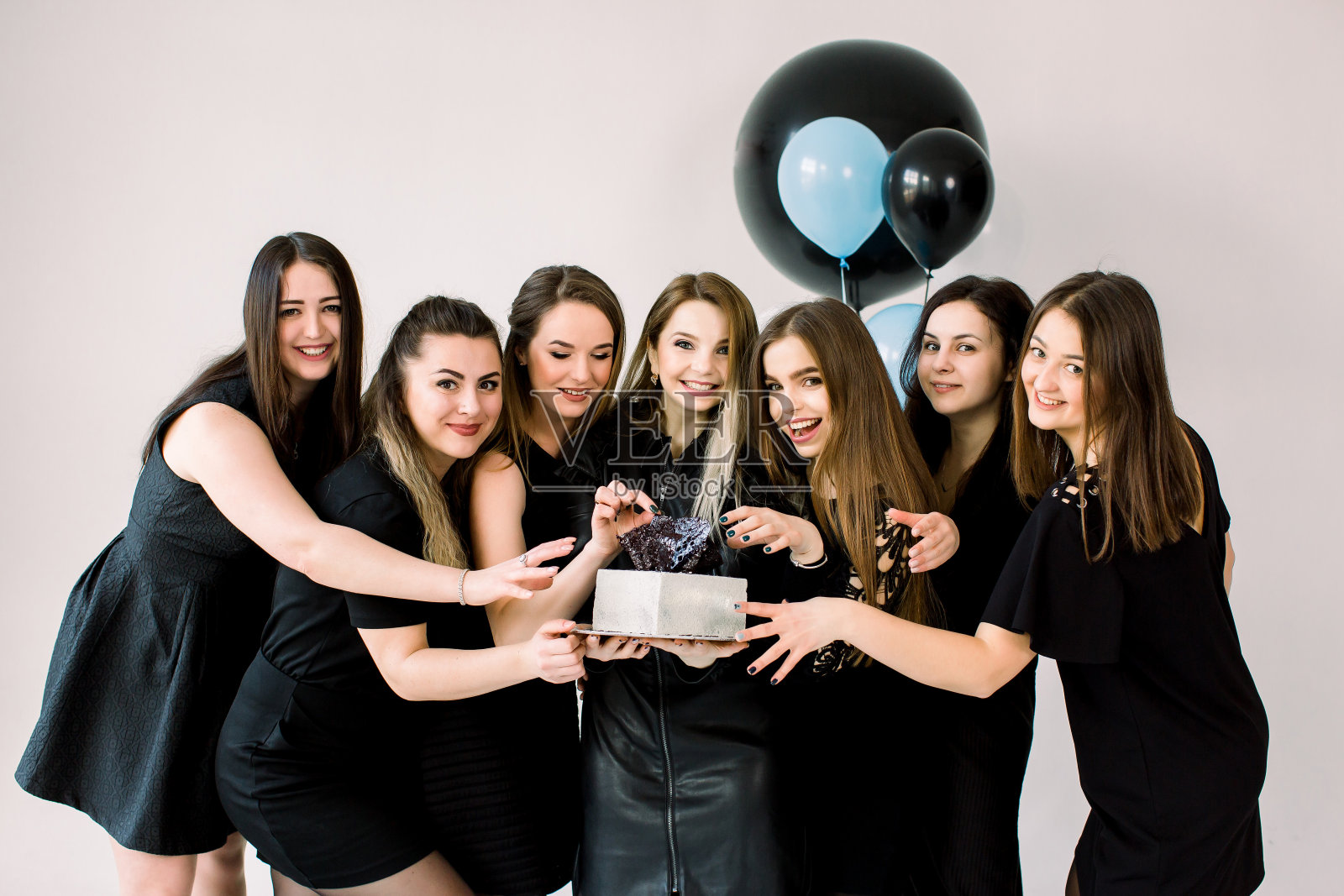 年轻的女士们穿着黑色礼服在工作室庆祝生日。女孩最好的朋友有乐趣拿着生日蛋糕和微笑。生日派对、节日、妇女节概念照片摄影图片