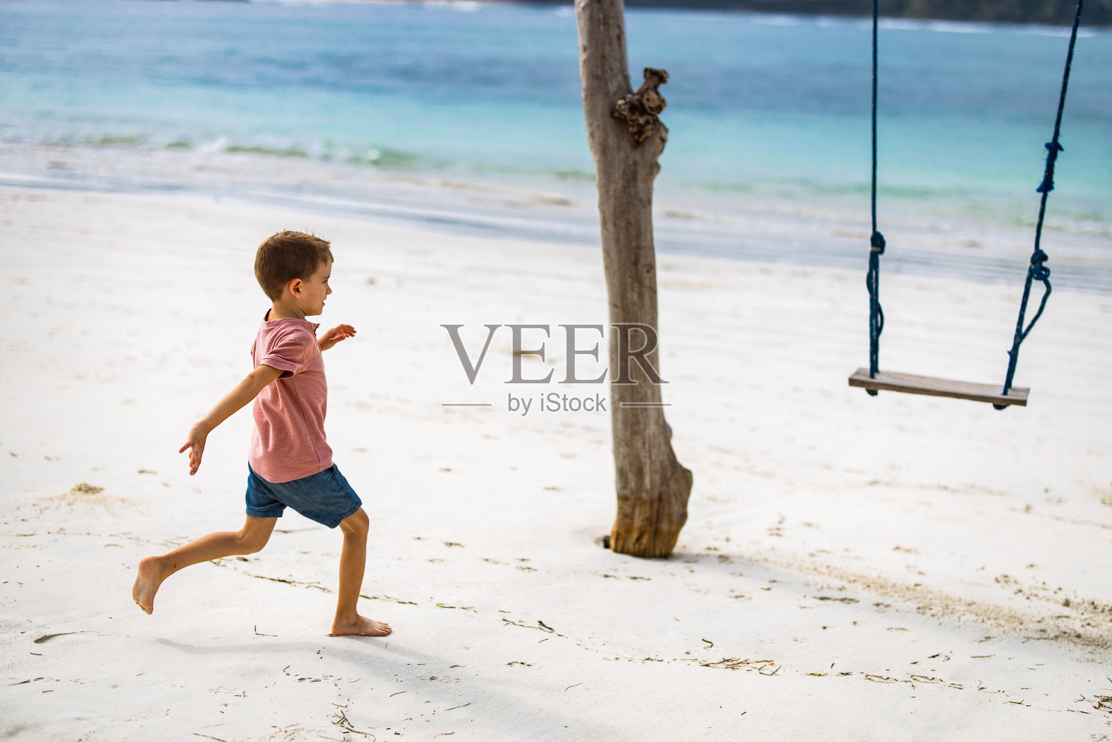 快乐的男孩朝海滩上的秋千跑去。照片摄影图片