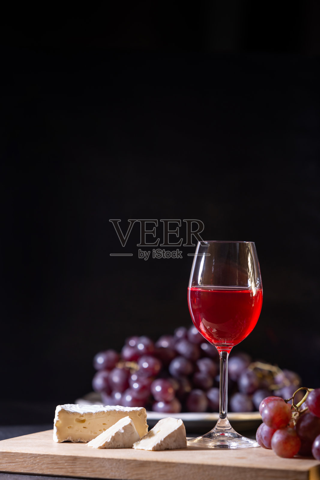 一杯红果酒。葡萄和布里干酪的特写在一个低基调的深色背景上。照片摄影图片