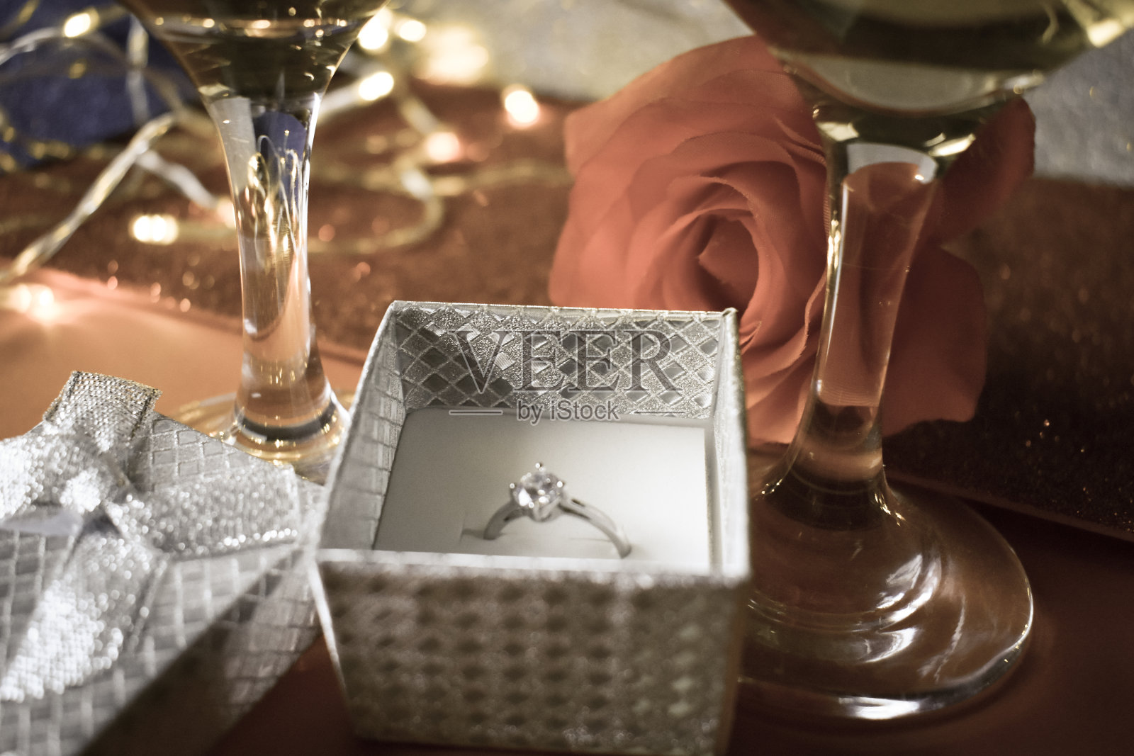 一个里面有订婚戒指的盒子，旁边放着一朵玫瑰和两杯酒。照片摄影图片