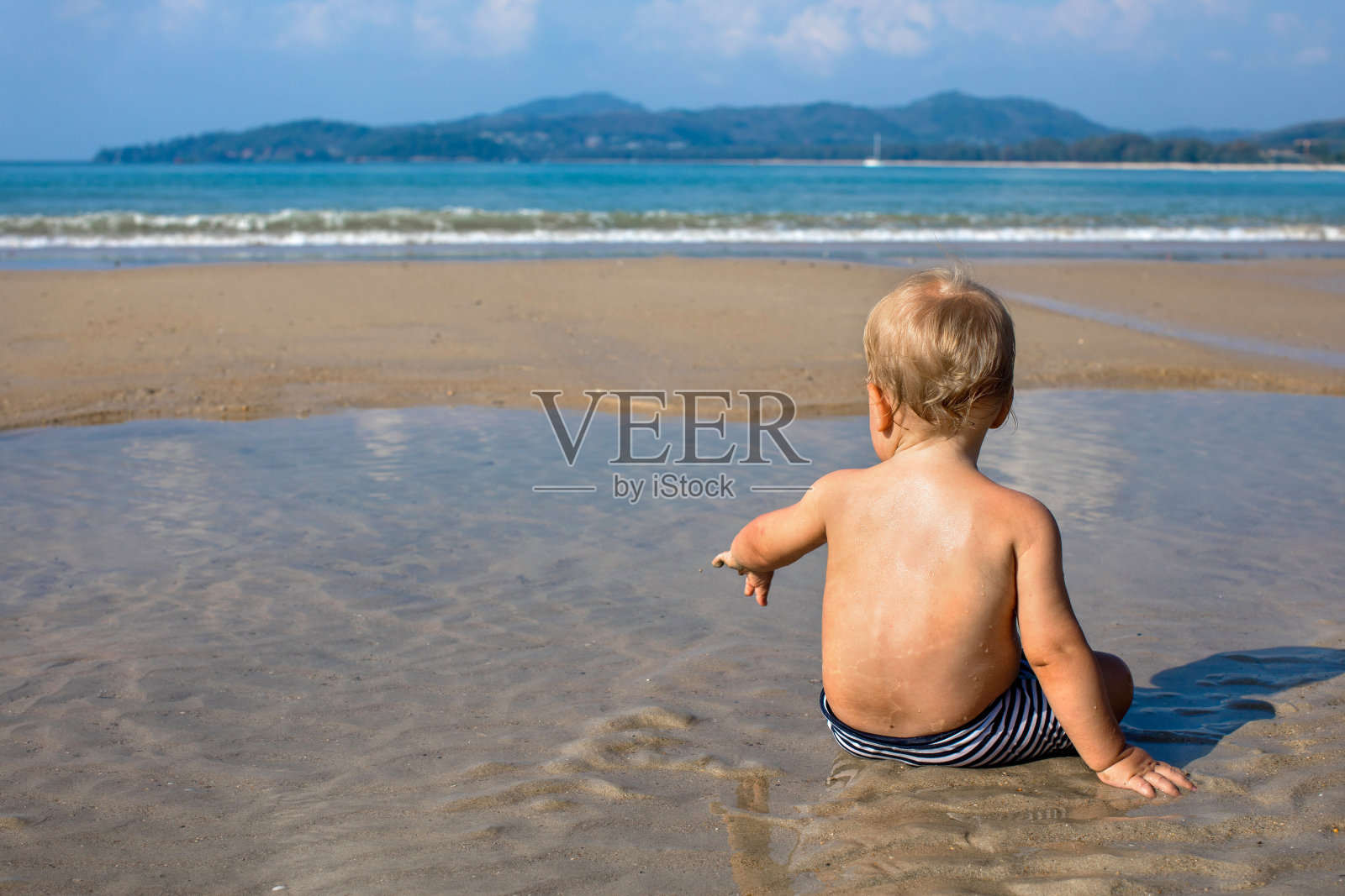快乐的小孩坐在海边的水在夏天的背影照片摄影图片