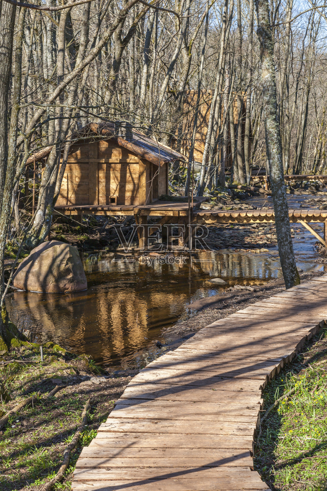 春天的森林里，河边有一座人行桥的小木屋照片摄影图片
