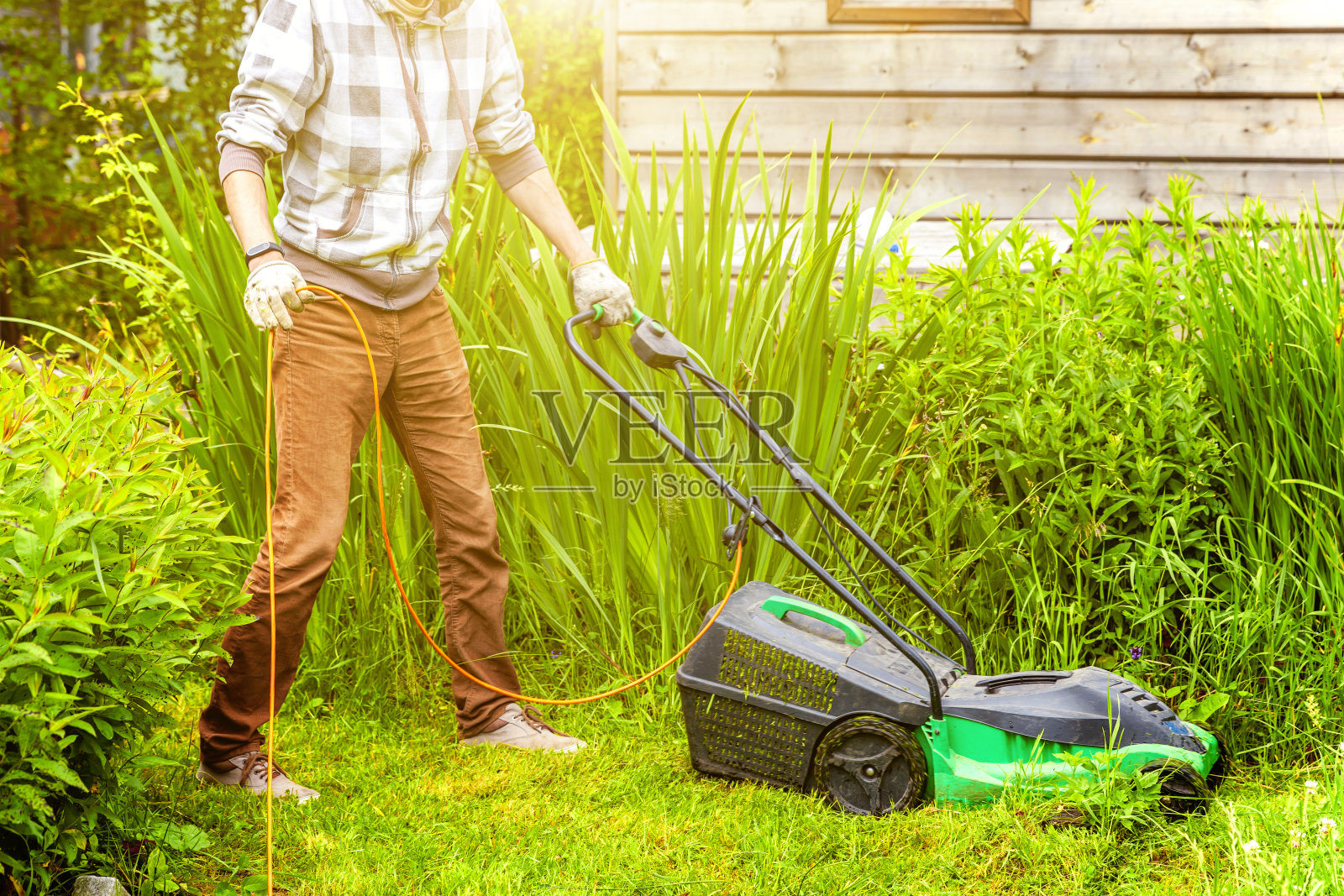 一个人在后院用割草机割绿草。园艺乡村生活背景。在春天或夏天的季节，在阳光下的新鲜的绿色草地草坪，花园景观美丽的景色照片摄影图片
