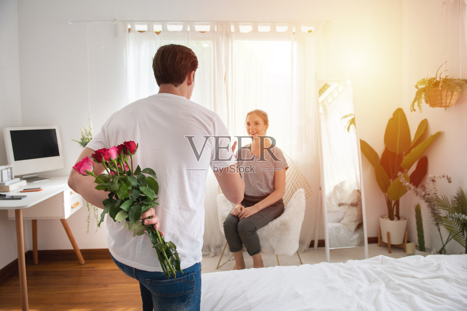 日常生活中的意外时刻!照片的男人的手隐藏着别致的红玫瑰与背后，幸福的女人是模糊的背景与复制空间照片摄影图片