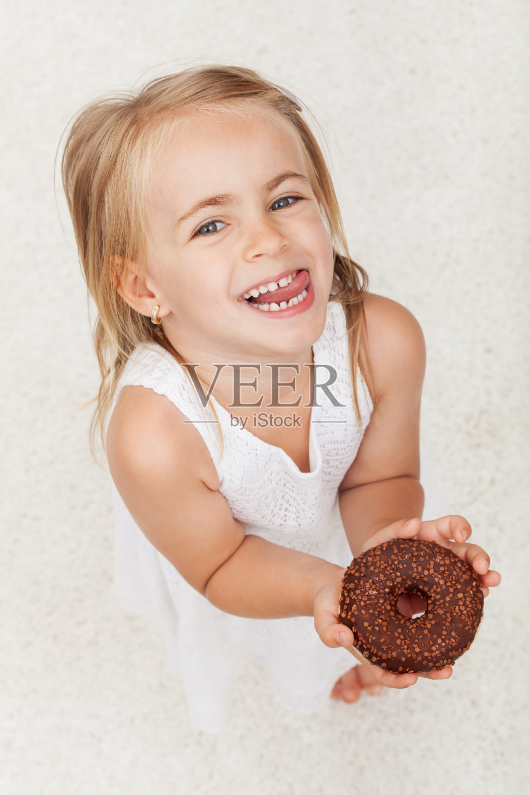 快乐的小女孩拿着一个巧克力甜甜圈-看着一个灿烂的微笑照片摄影图片