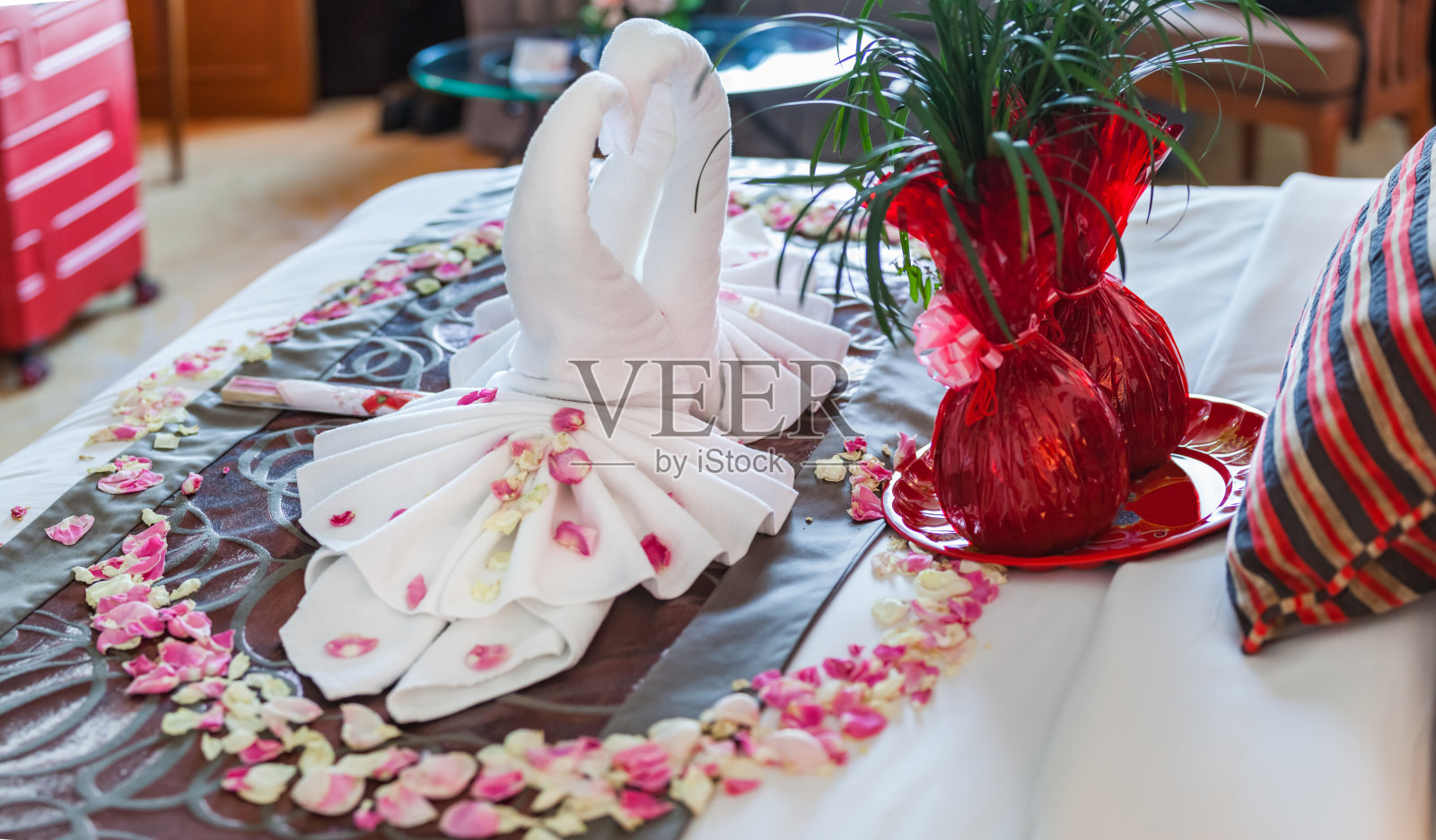 浪漫的卧室内饰，亲吻天鹅折纸毛巾和洒在床上的新鲜粉白玫瑰花瓣装饰。婚礼，周年纪念，蜜月，爱，象征概念照片摄影图片
