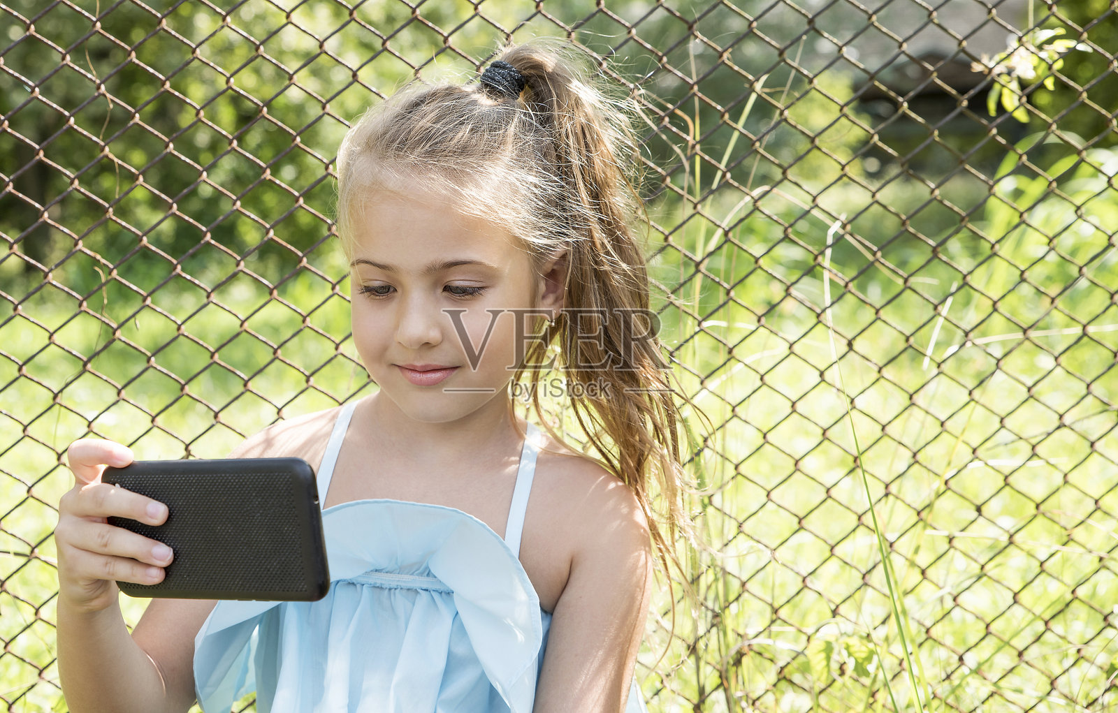可爱的小女孩坐在公园里看智能手机照片摄影图片