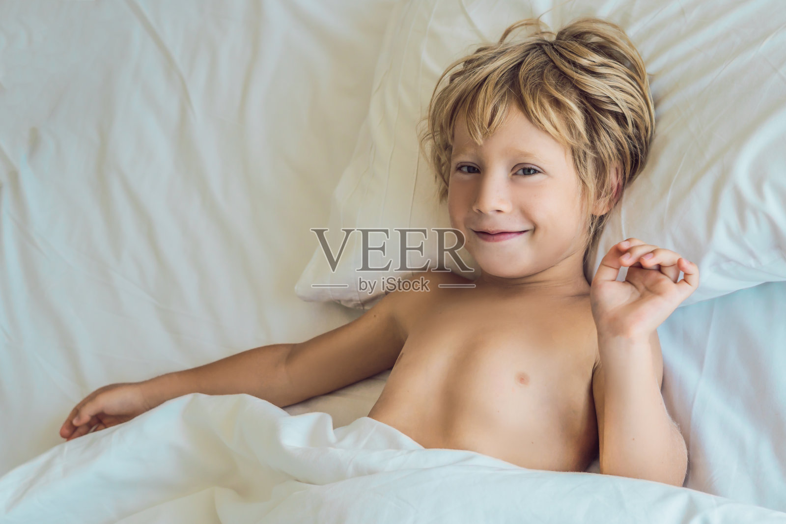 在床上微笑的男孩在他的床上醒来照片摄影图片