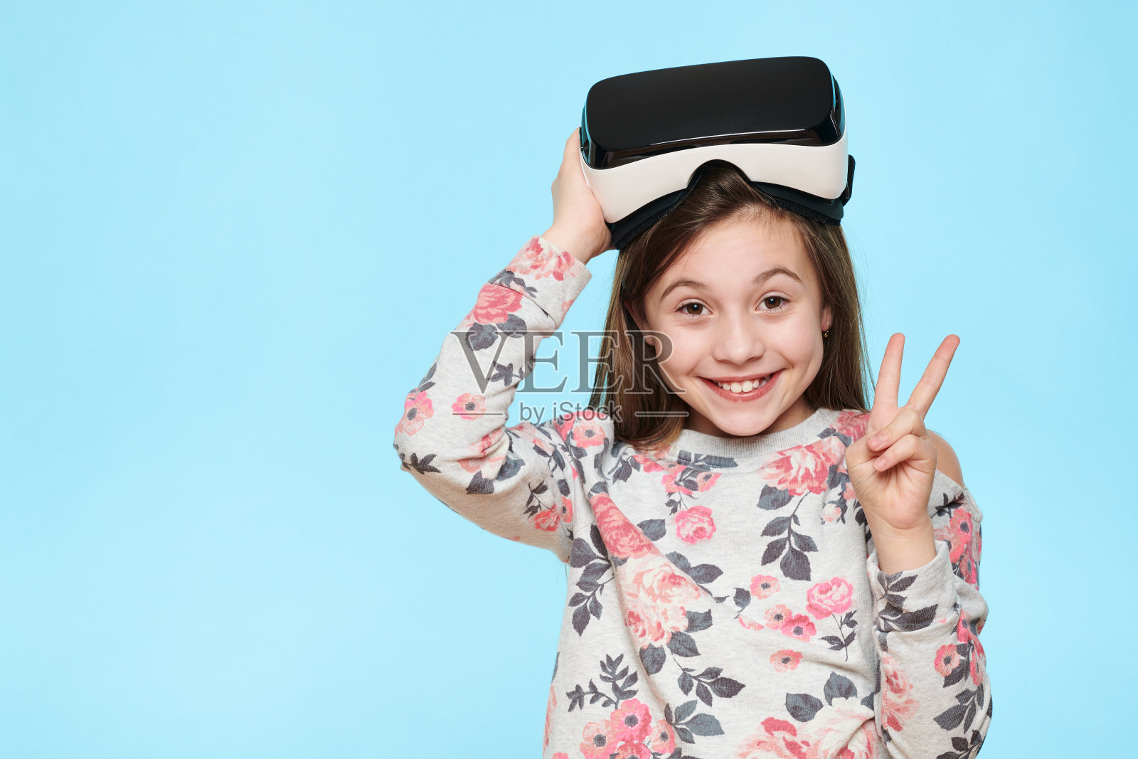 工作室肖像可爱的年轻白人女孩戴着虚拟现实眼镜在淡蓝色的背景。未来的小工具技术概念。照片摄影图片