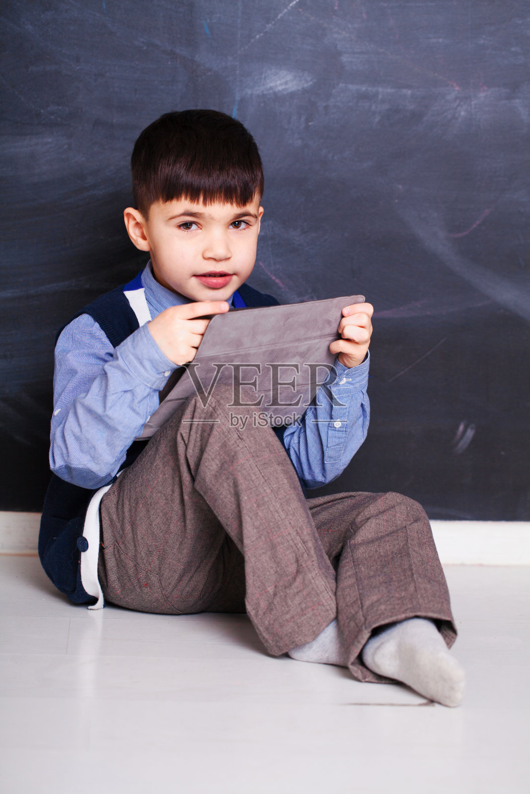 快乐的小男孩坐在地板上用平板电脑。照片摄影图片