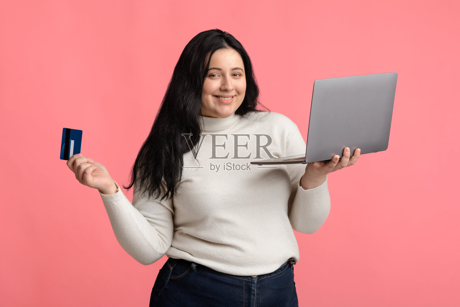 快乐的丰满女人与笔记本电脑和信用卡在粉红色的背景照片摄影图片