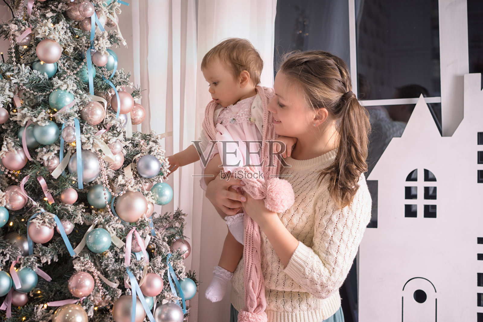 一位年轻的母亲在圣诞树前抱着一个一岁的女儿照片摄影图片