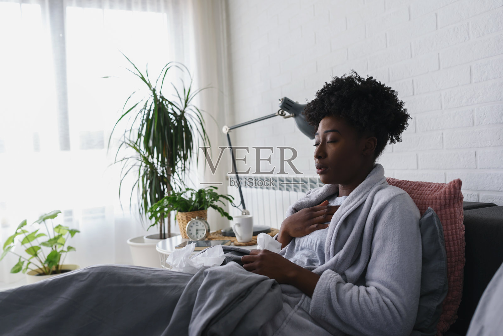年轻的非裔美国妇女躺在家里的床上。得了流感，生病了。照片摄影图片