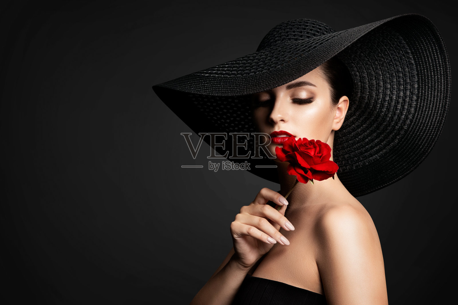 美丽的女人和红花，优雅的女士在黑宽宽边帽闻玫瑰照片摄影图片