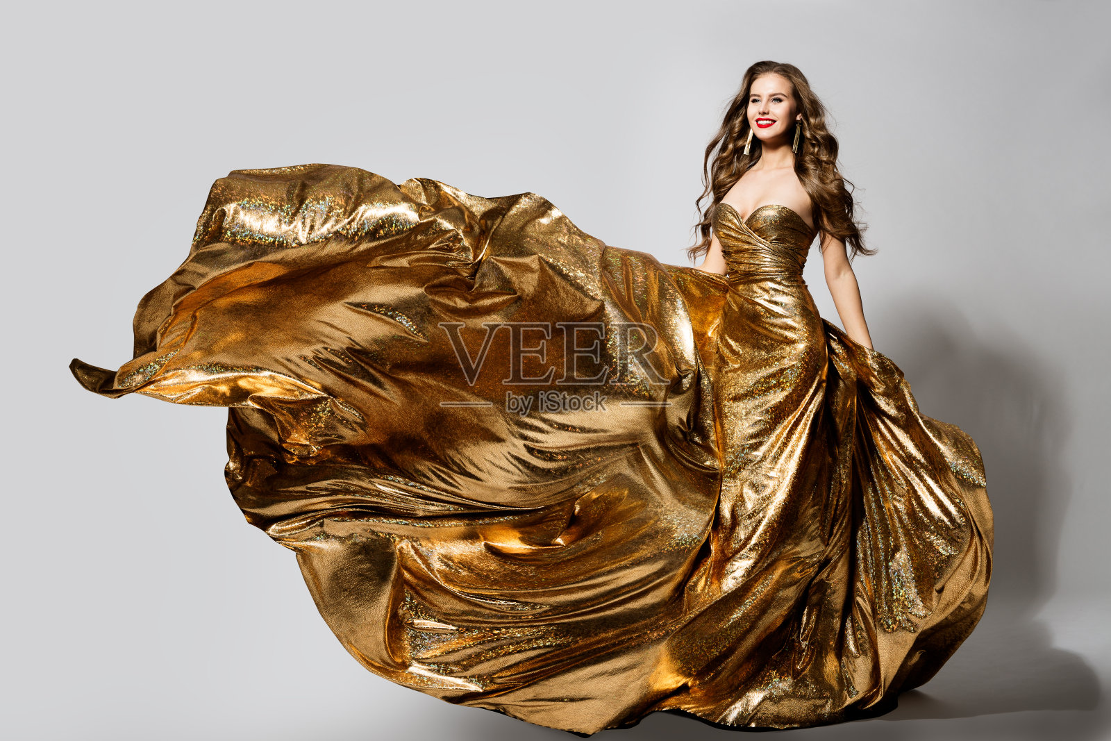 在风中飘扬的金色长裙，快乐美丽的女士在飘扬闪闪发光的金色长裙照片摄影图片