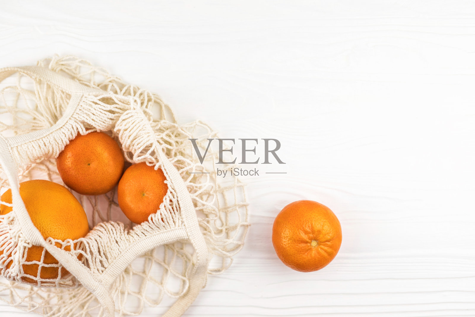 橘子和橙色在一个网眼袋在白色木制背景。照片摄影图片