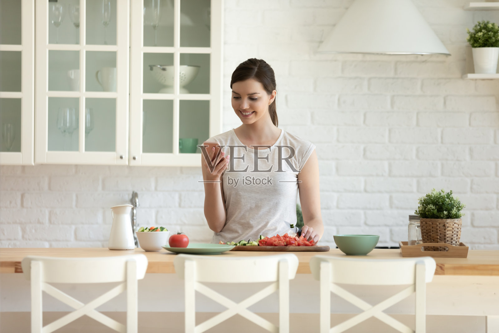 快乐的年轻女子烹饪在智能手机上阅读食谱照片摄影图片