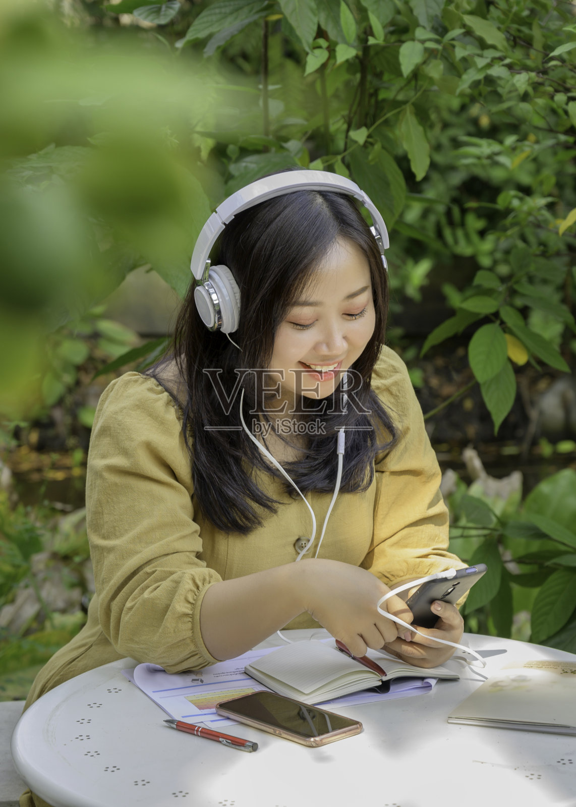 美丽开朗的女士戴着耳机听音乐，在花园里放松。照片摄影图片