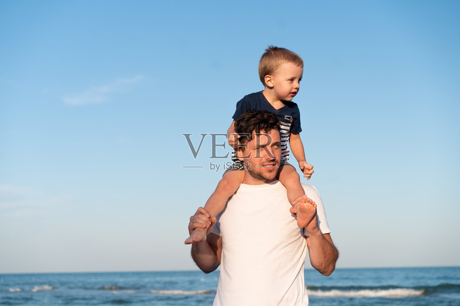 炎炎夏日，年轻的白人爸爸带着小儿子沿着海边散步。暑期家庭度假概念。父子友谊。照片摄影图片