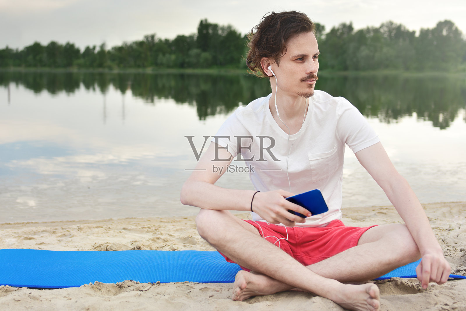 一个男人坐在湖边的海滩上听着音乐照片摄影图片