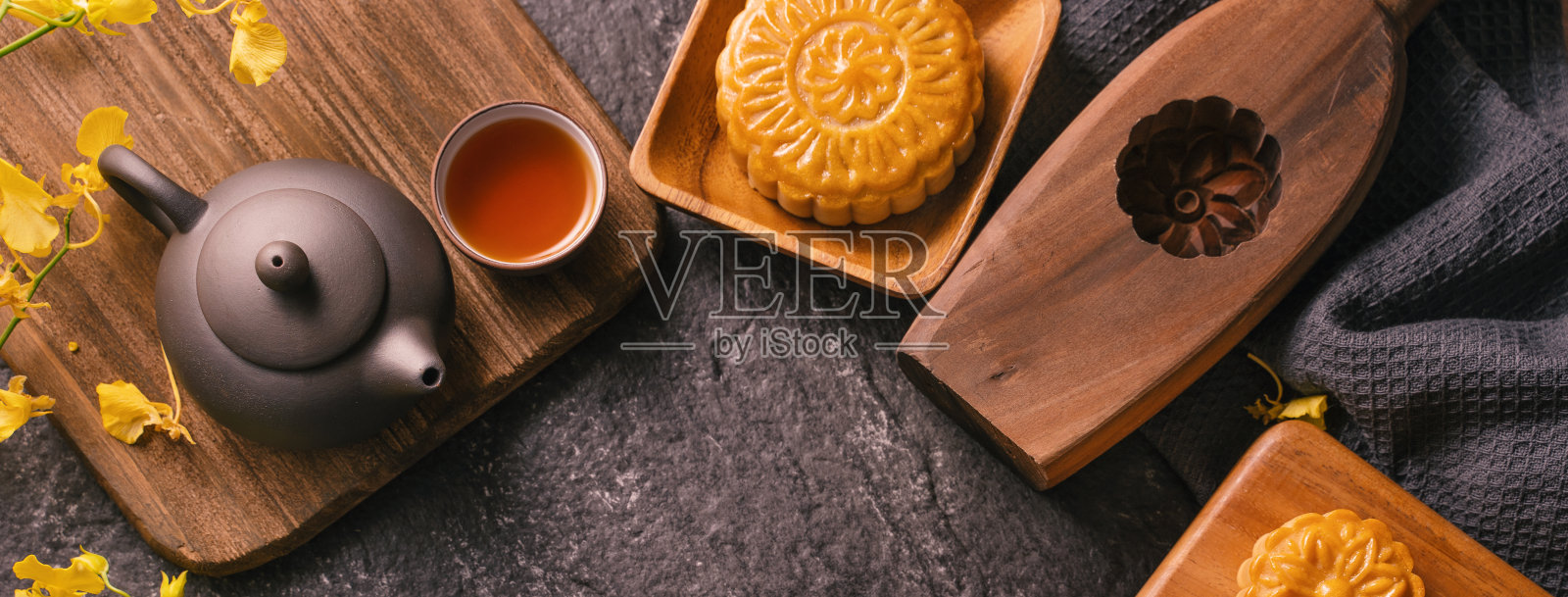 中秋节传统食品概念-美丽的月饼在黑石板桌上用茶，糕点模具，花。照片摄影图片