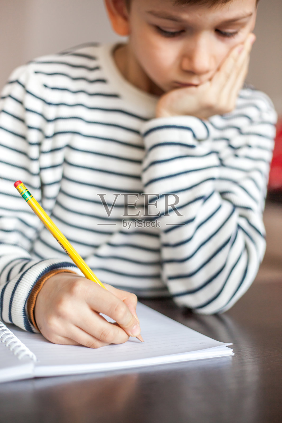 一个7岁的男孩拿着黄色的铅笔，集中精力做作业的特写照片摄影图片
