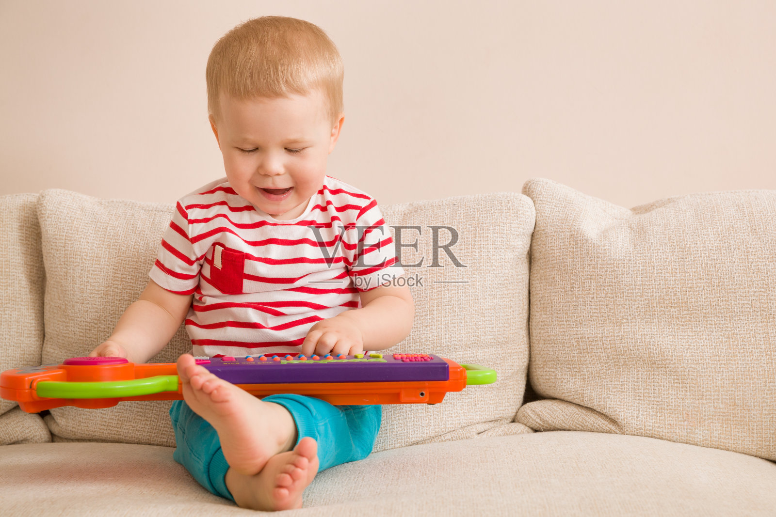 可爱的小男孩坐在沙发上玩玩具钢琴的肖像。在家早期学习。小音乐家。孩子,toys.Education。在室内。照片摄影图片