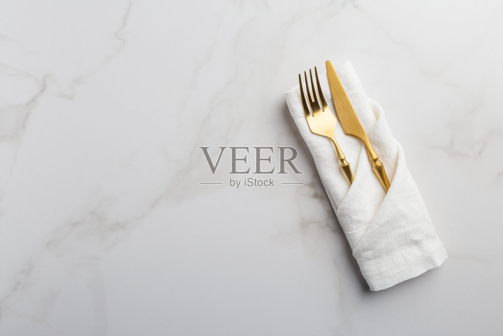 白色大理石背景上的白色餐巾上的金色餐具照片摄影图片