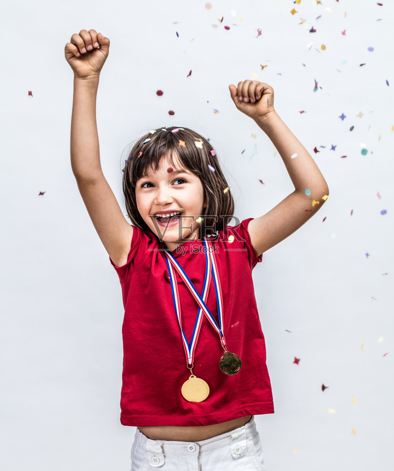 成功美丽的孩子笑着拿着冠军奖牌，在五彩纸屑上庆祝照片摄影图片