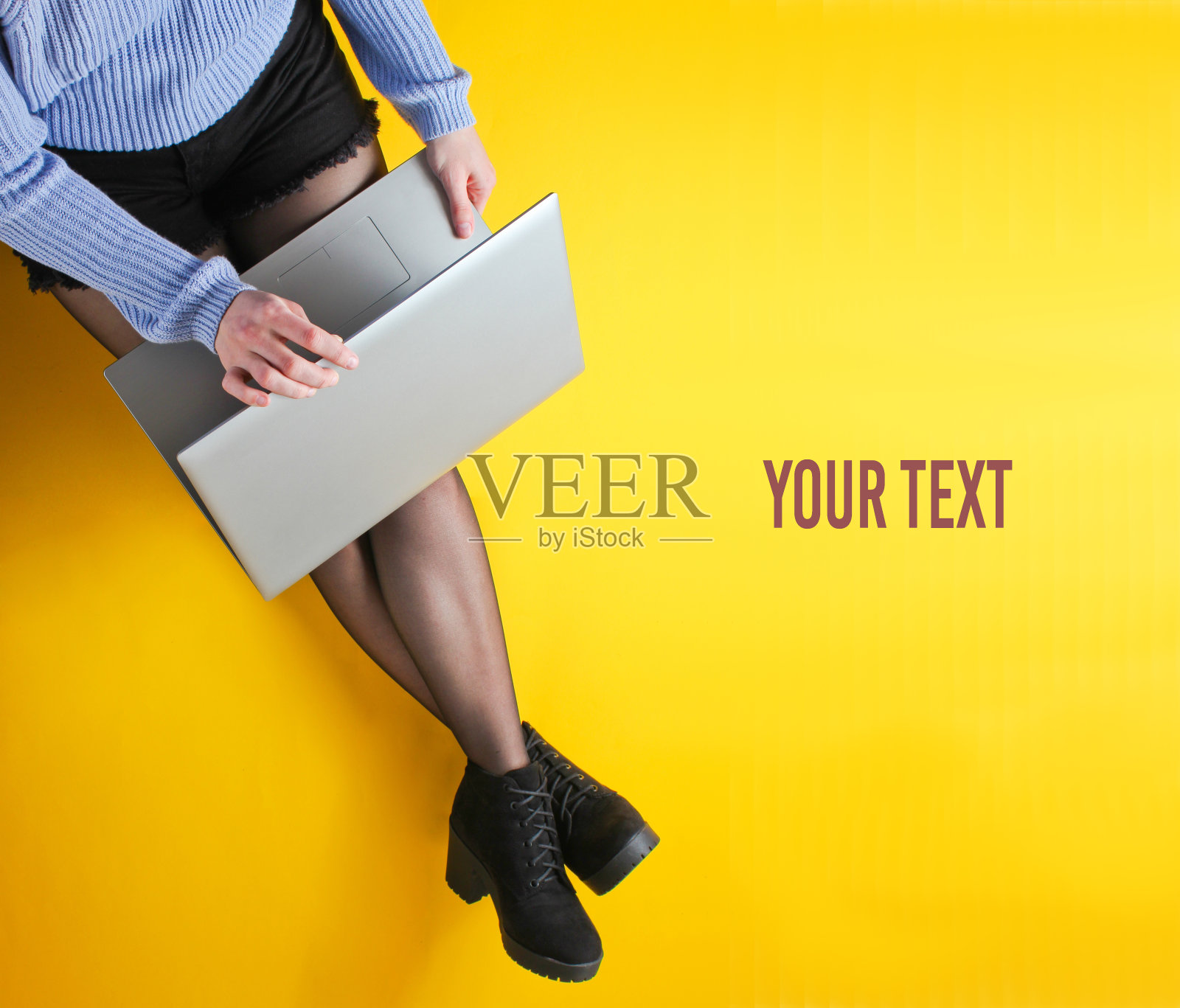 一位穿着短裤、紧身裤和靴子的商务女性正坐在黄色的背景上在笔记本电脑上打字，屏幕上留有文本空间。自由职业者，博客，在线工作者的概念。俯视图照片摄影图片