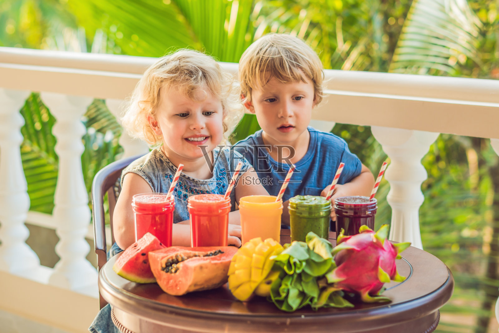 孩子们喝多彩的健康果汁…西瓜、木瓜、芒果、菠菜、火龙果。冰沙，果汁，饮料，各种饮料和新鲜水果在木桌上照片摄影图片