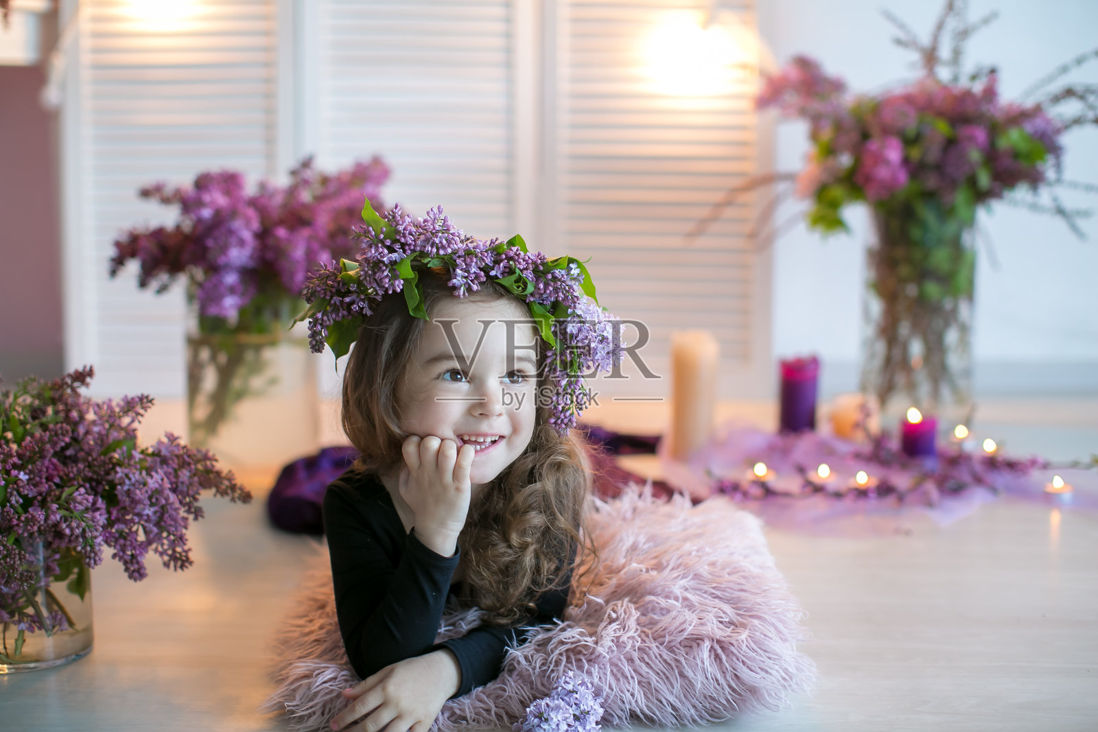一个头上戴着丁香花环的小女孩坐在地板上，周围放着一瓶花照片摄影图片
