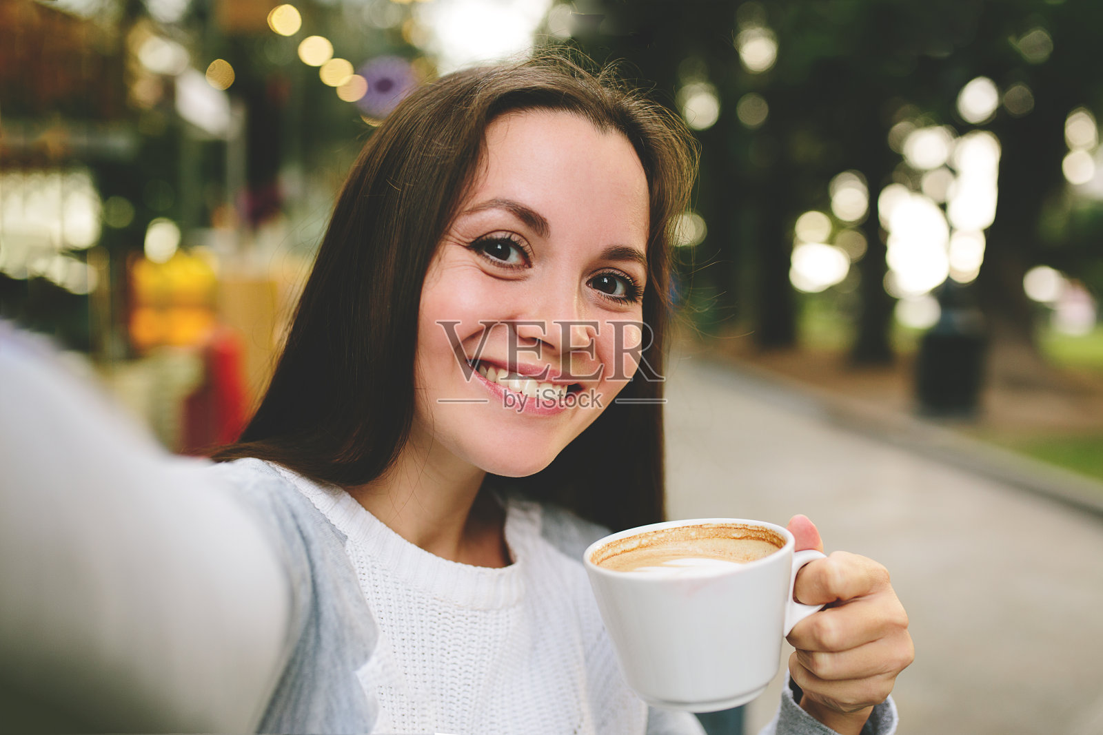 年轻漂亮的女孩喝着咖啡，在街头咖啡馆自拍照片摄影图片