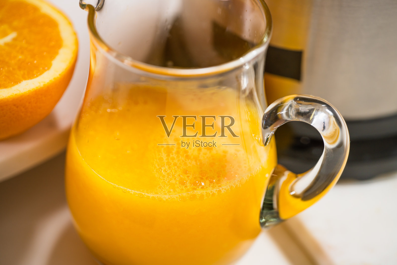 鲜榨橙汁在一个玻璃罐子靠近白色的背景。用电动榨汁机准备新鲜橙汁照片摄影图片