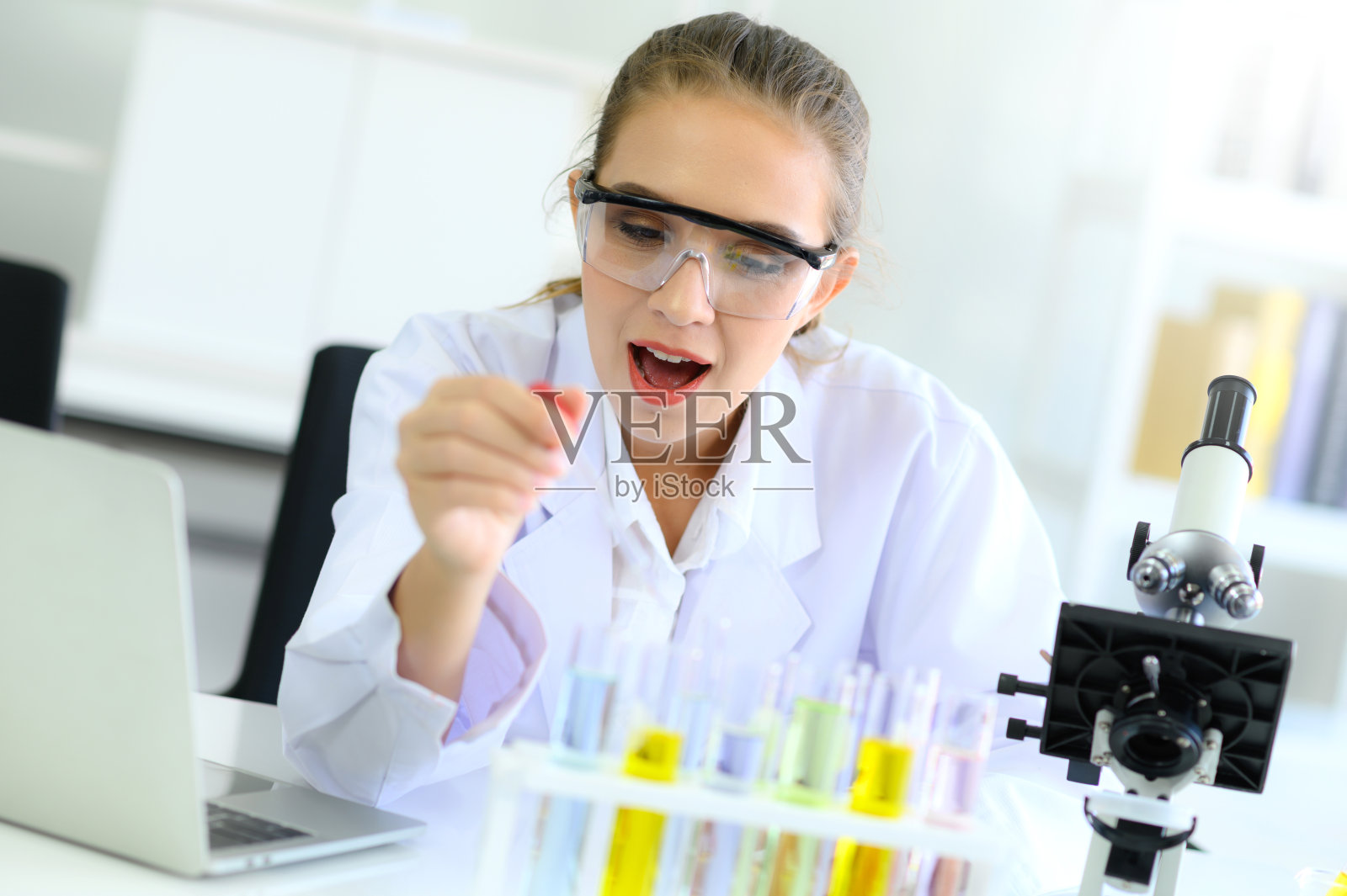 年轻的女科学家兴奋地在实验室里用显微镜、试管、滴管和笔记本电脑做实验照片摄影图片