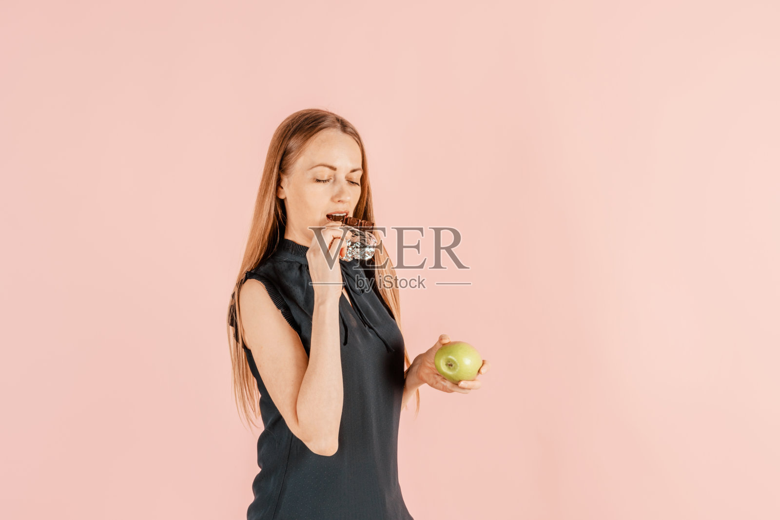 饮食,健康饮食。这个女孩手里拿着一个苹果和巧克力。选择正确的营养的概念。困难的饮食。素食者。照片摄影图片